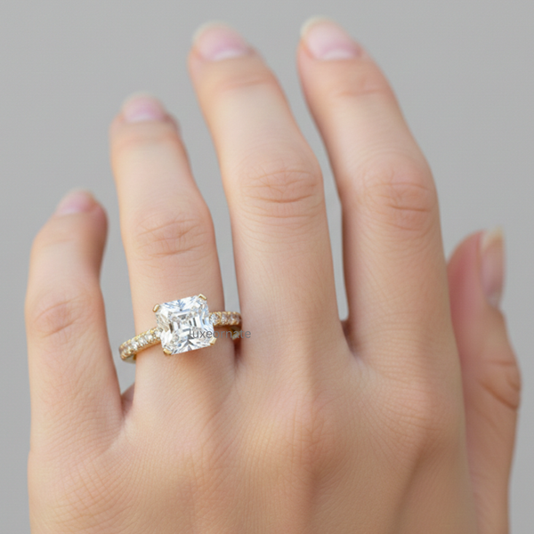 Emerald cut lab grown diamond engagement ring in yellow gold on woman’s hand, rectangular step cut solitaire with pavé diamond band, four prong setting, luxury bridal jewelry.