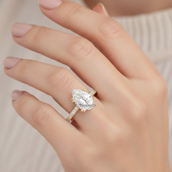 Pear shaped diamond engagement ring in yellow gold with pavé split shank band worn on hand.