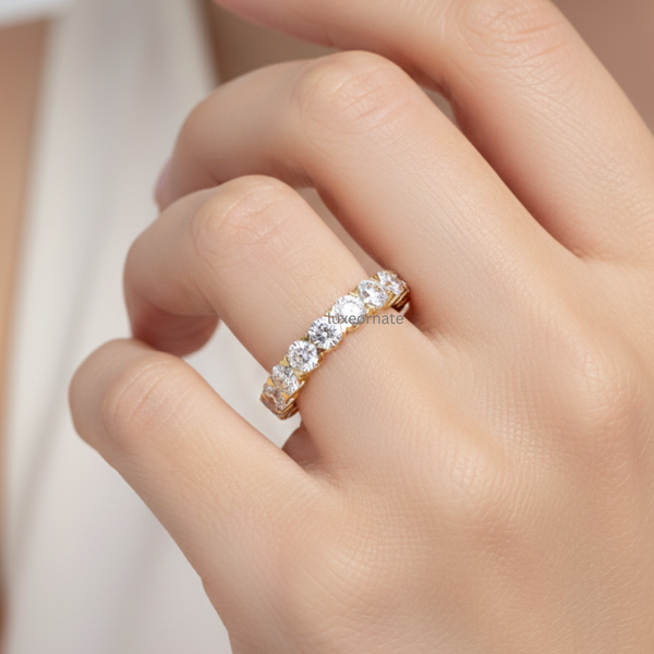 Round brilliant lab grown diamond eternity band in yellow gold on woman’s hand, full shared prong wedding ring, anniversary band, luxury fine jewelry.